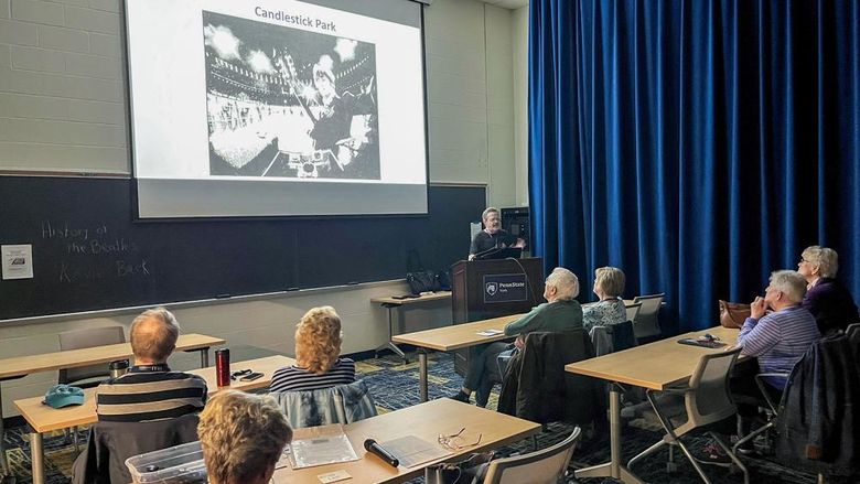 Back view of a classroom of older people at desks and a photo on the screen with instructor at front