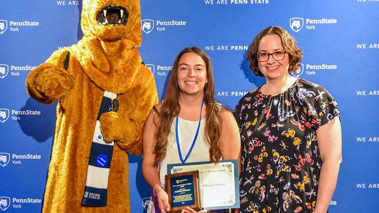 Nittany Lion with female student and female faculty member displaying an award.