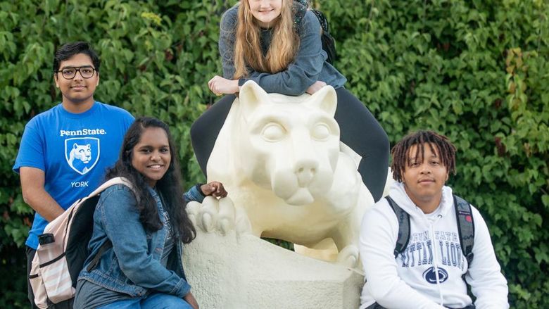 Four students, two males and two females, sitting on and around the Nittany Lion Shrine