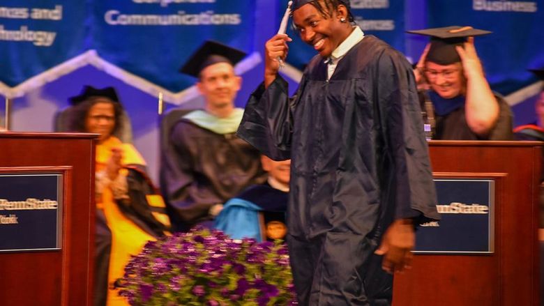 African American student in cap and gown crossing the stage and grabbing tassel at commencement