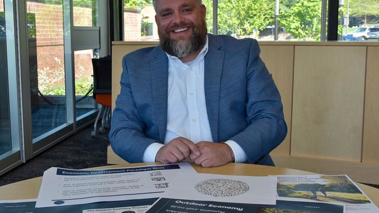 Bearded white male dressed in a suit showing off materials on the desk in front of him.