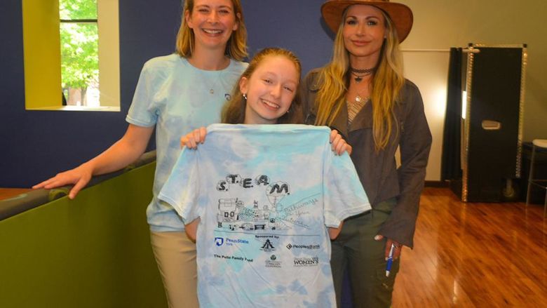 Three females, two older and a young student, show off a T-shirt design for the Pathways program.