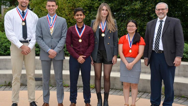 Three male and two female students pose with older gentleman wearing glasses