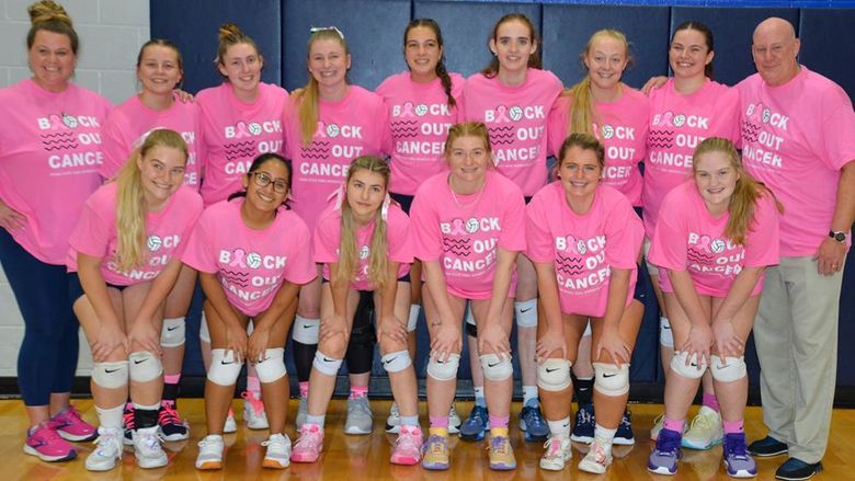 Two adults, female and male, along with thirteen female volleyball players wearing pink T-shirts