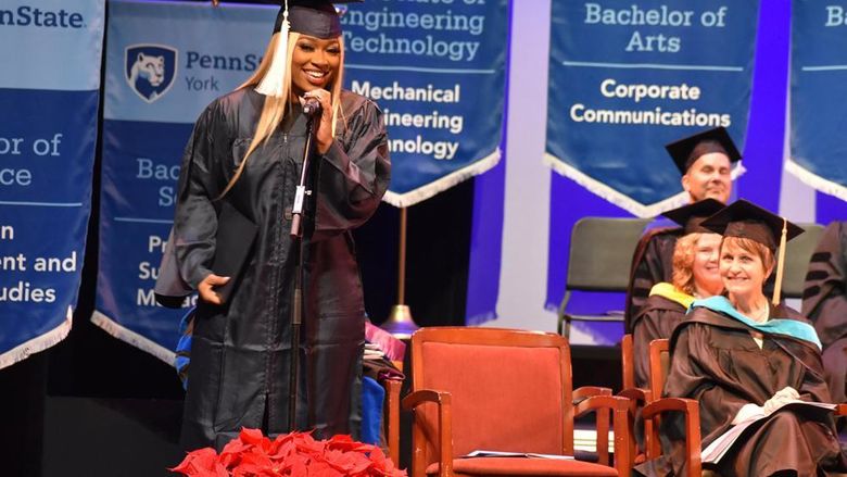 African Amercian female with long hair at microphone during commencement ceremony