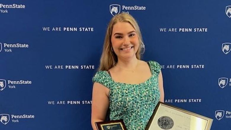 Person smiling, holding plaques, standing in front of blue backdrop.