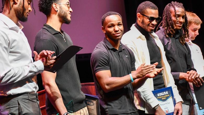 Young men stand in a line on a stage, some holding awards, some clapping.