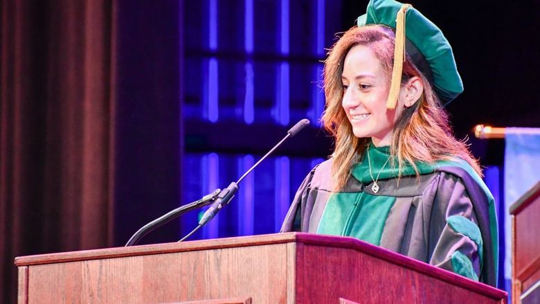 Woman in regalia speaks at a podium.