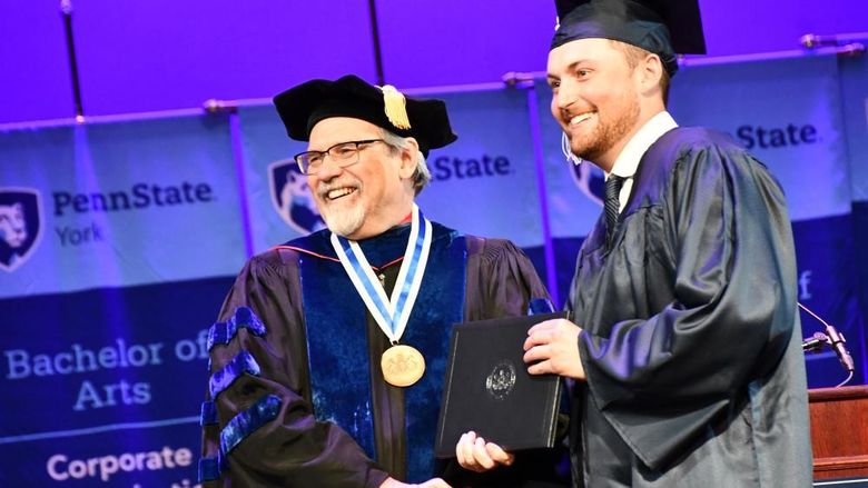 Two men in regalia shaking hands at a graduation ceremony. 
