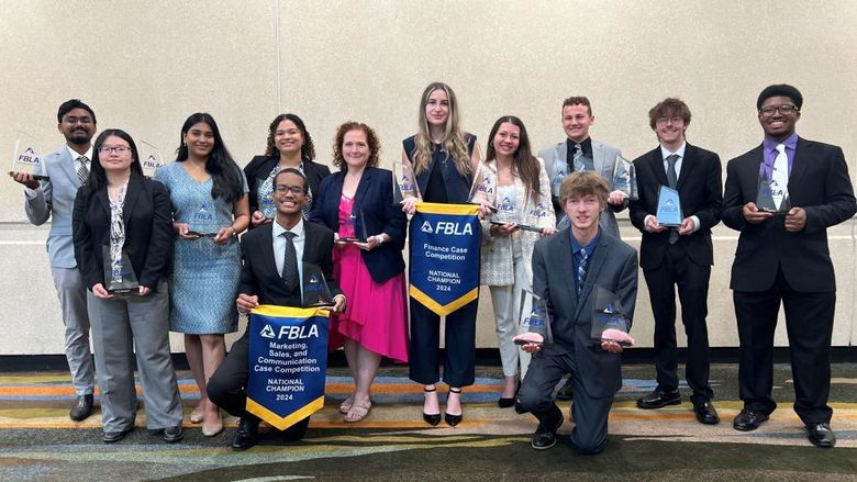 A group of students stand with a faculty member, showing off awards.