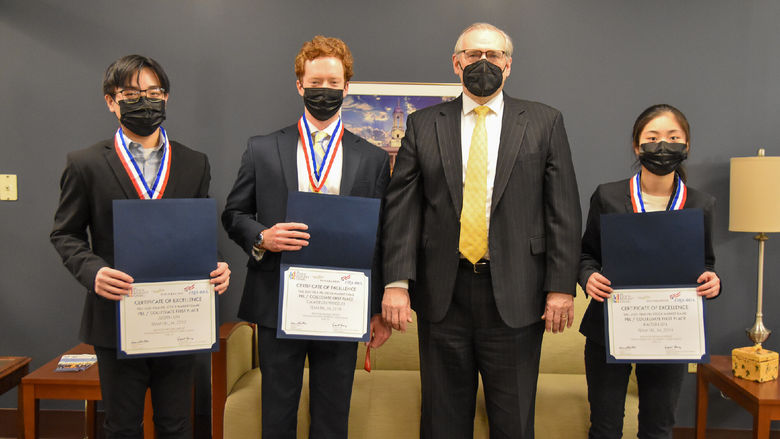 Four people, three students, and one adult, pose for a photo with certifcates for a first-place win in a national competition 