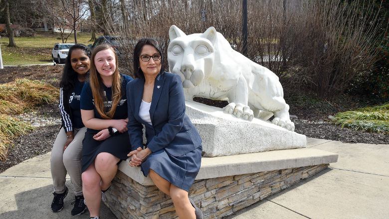 Two female students and an older female sit together by the Nittany Lion Shrine at Penn Stae York. 