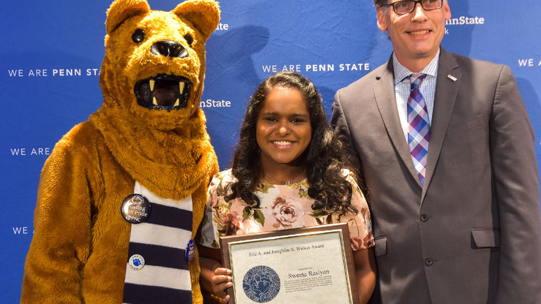 Person in Nittany Lion suit with female award recipient and male presenter at awards program.