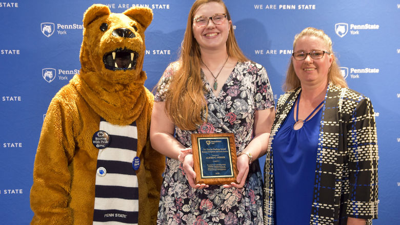 Person dressed in Nittany Lion costume and two femailes with glasses are opart of an award presentation.