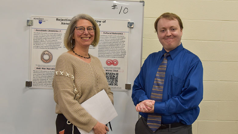 Female faculty member, wearing glasses, and male stuent at display board