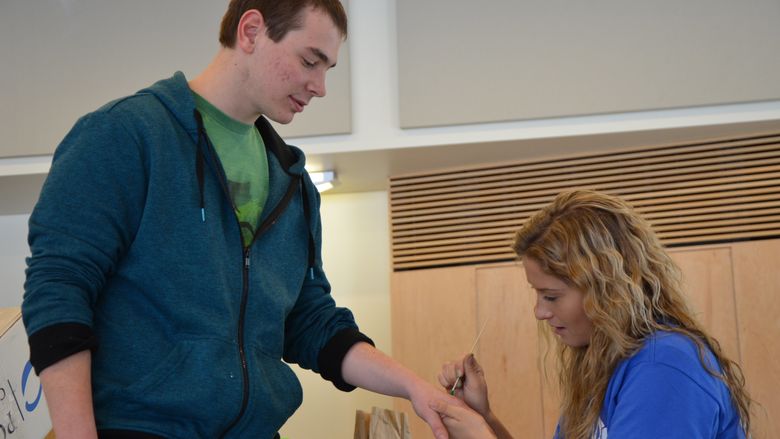 A student painting a green dot on another student's hand