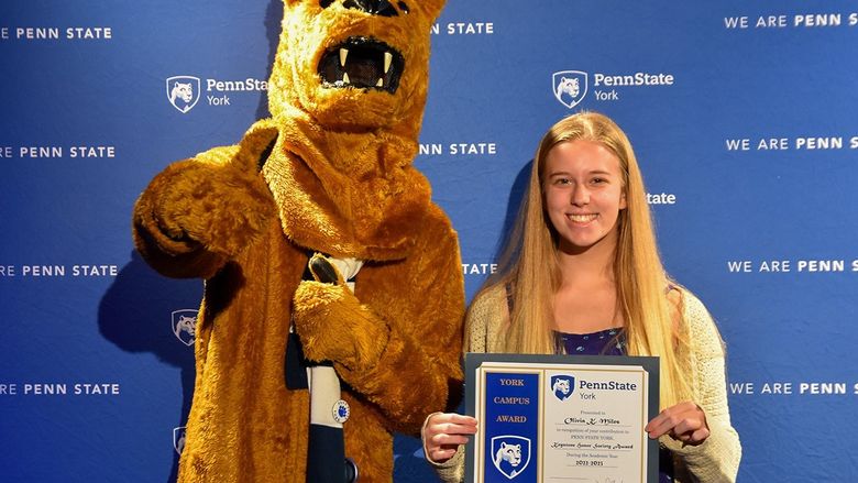 The Nittany Lion mascot standing next to a female student who is holding a certificate.