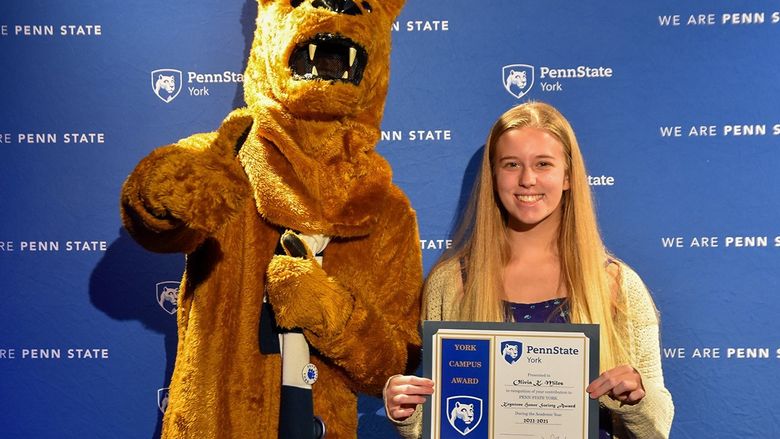 The Nittany Lion mascot standing next to a female student who is holding a certificate.