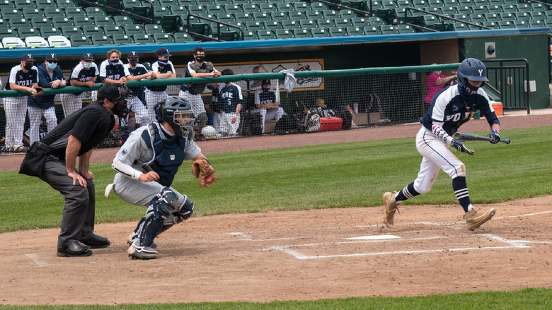 Baeball player swinging bat, catcher and umpire at stadium