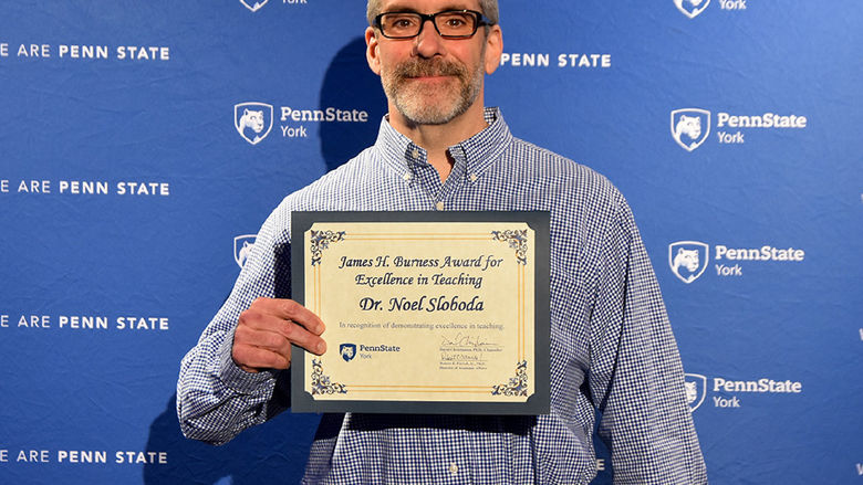 Male faculty member wearing glasses and holding a certificate.