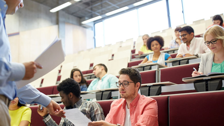Professor hands papers to students in a lecture hall.
