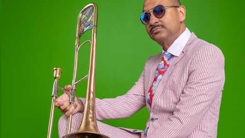 Delfeayo Marsalis wearing sunglasses and a pinstripe suit and holding a trombone