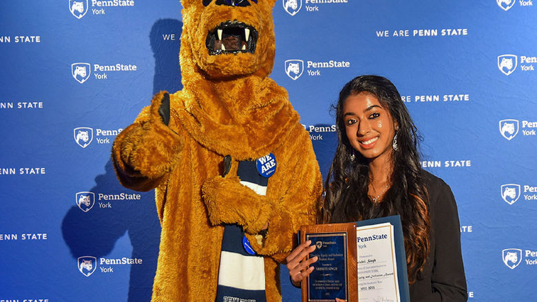 Nittany Lion character with female student of color holding an award.