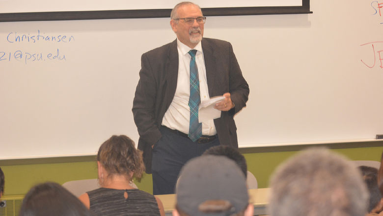 Older adult Caucasian male wearing a suit and glasses talking to a group