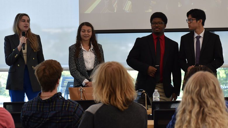 Two females and two males dressed in business attire in front of a group