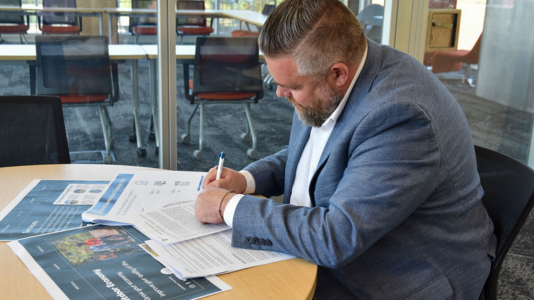 Man in a suit at a table writing on documents.