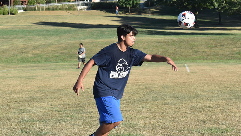 Male soccer player runs with a soccer ball in the air.