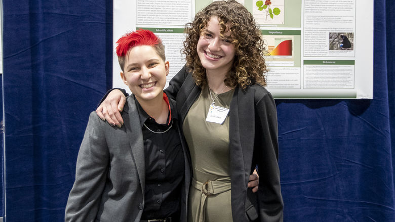 Two students pose in front of a poster about invasive species at the regional symposium