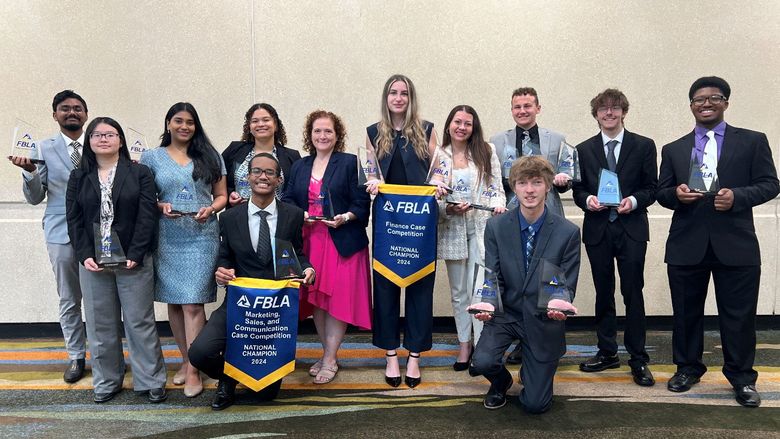 A group of students stand with a faculty member, showing off awards.