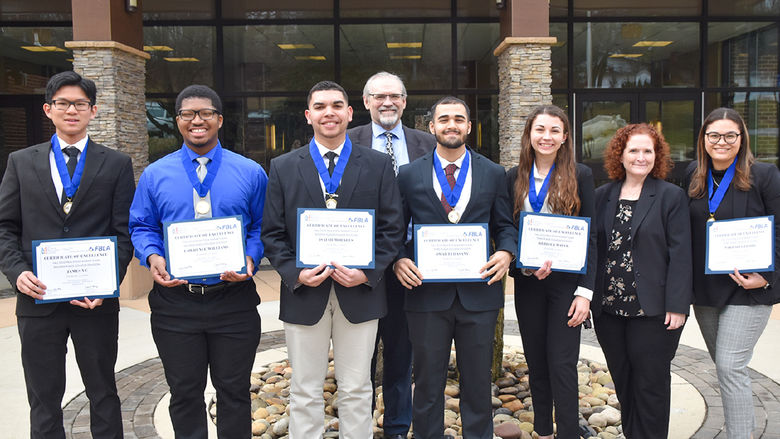 Eight males and females pose with awards in front of building.