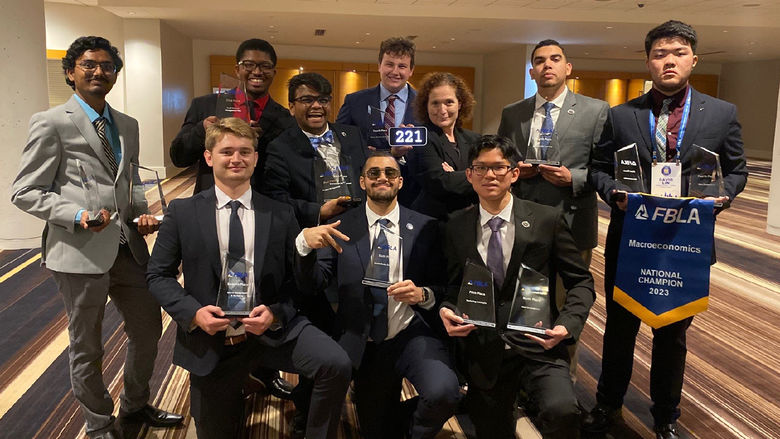 A group of nine students, holding awards, stands with their faculty member and adviser