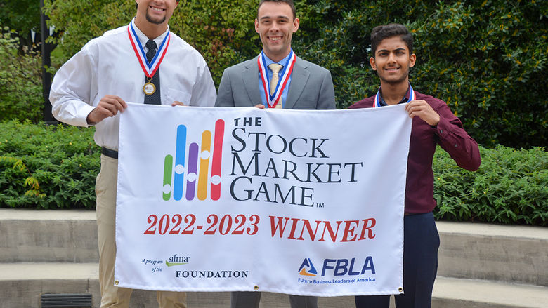 Three male students holding banner.