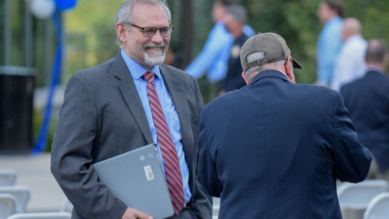 A man wearing a suit, holding a binder and smiling.