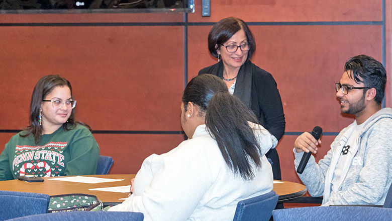 A student speaks into the microphone as a professor and other students listen.