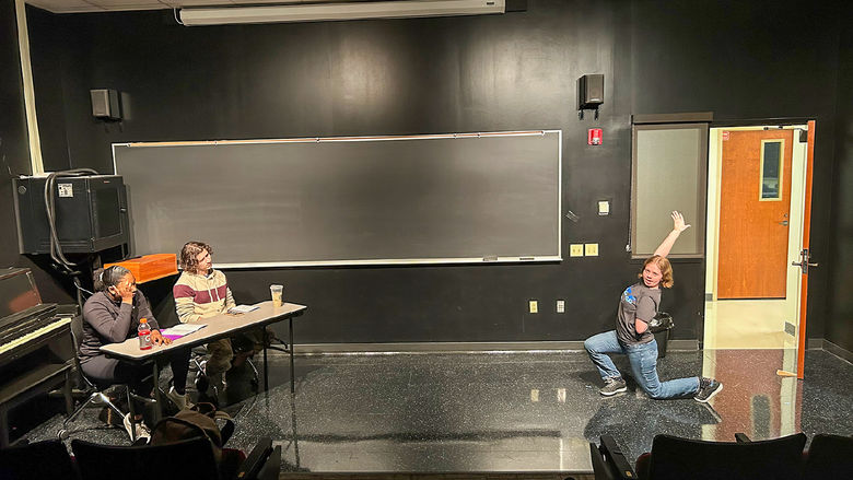 Male and female student at a table, other female student appearing to dance