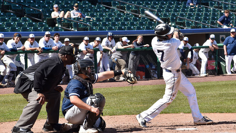 Umpire and catcher positioned behind a student in blue and white baseball uniform swinging a bat