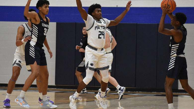 Basketball players on the court with one African American playing raising his arms to block a pass