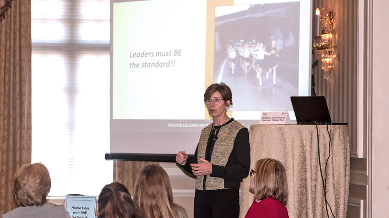 Retired Brigadier General Maureen LeBoeuf gives a presentation in a darkened ballroom.
