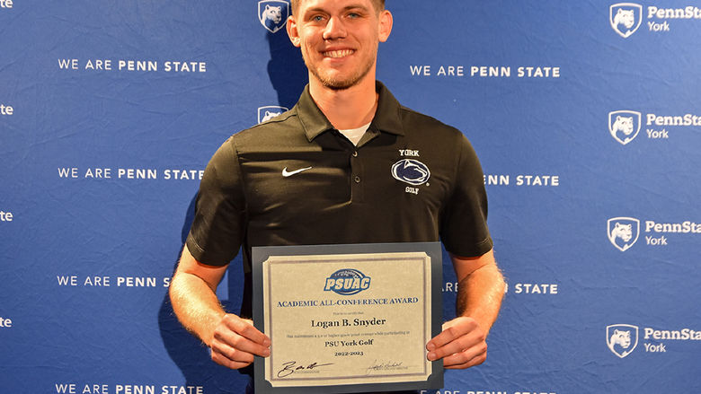 Male student-athlete holding an award certificate standing in front of a banner