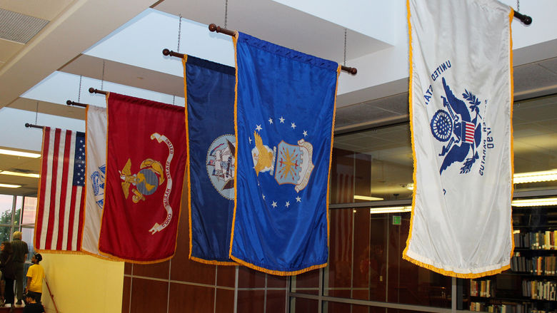 Military banners of several kinds are displayed alongside an American flag.