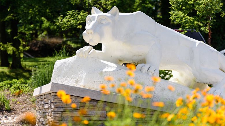 Nittany Lion Statue behind some orange summer flowers.