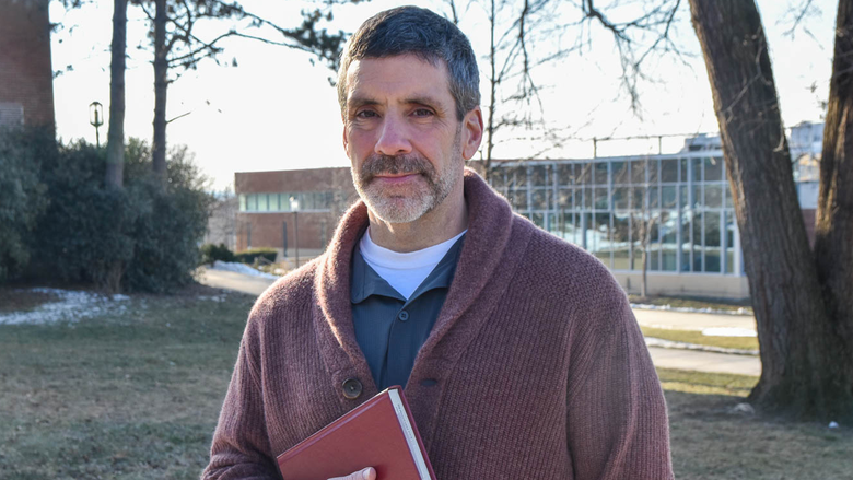 Bearded male standing outside holding abook