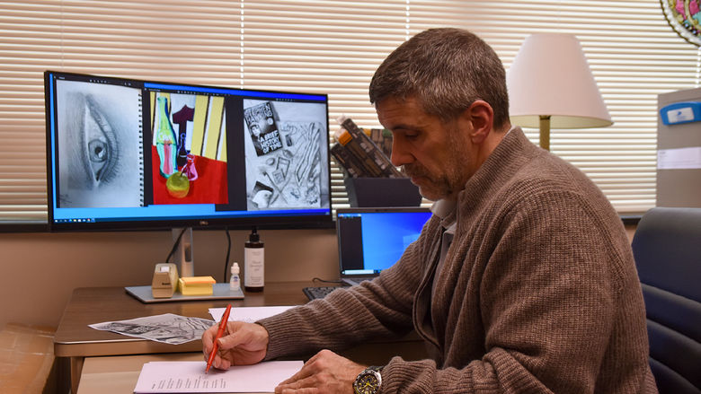 Man editing materials at a desk with visual art displayed on a computer screen