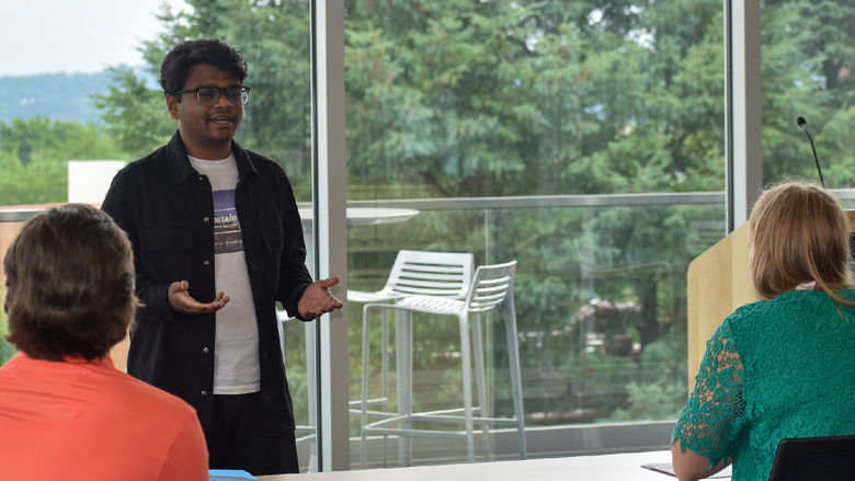 Young man standing in the front of a table presentaing to a male and female