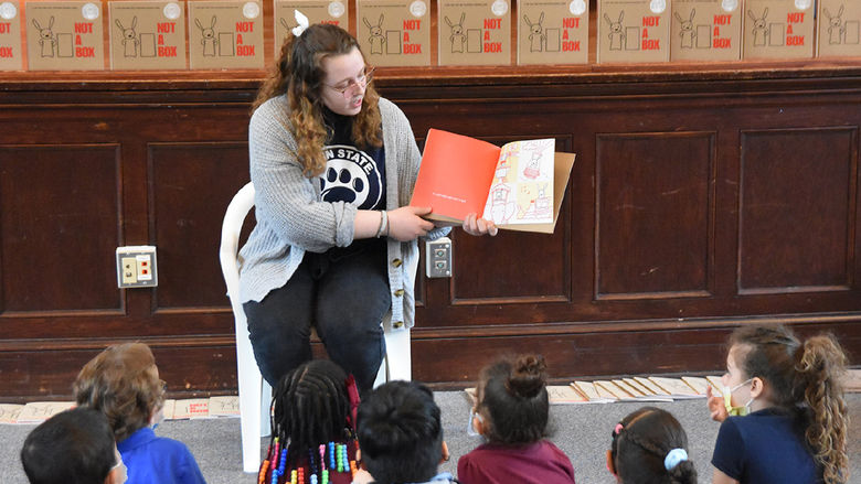 A Penn State York female student turns the pages of a book and reads to elementary school children.