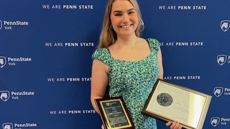 Person smiling, holding plaques, standing in front of blue backdrop.